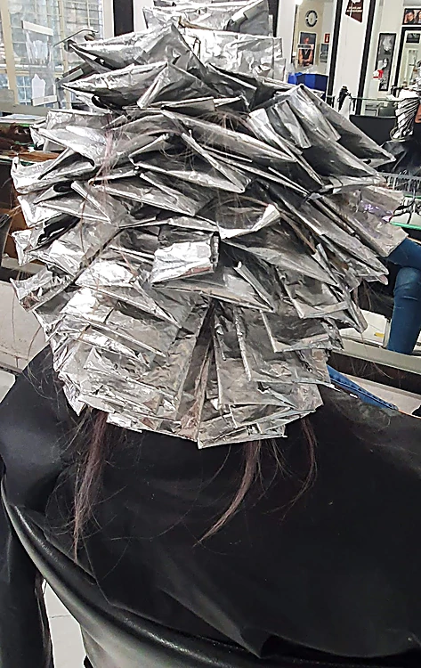 Cabeza de espaldas cubierta de papel aluminio en capas durante un proceso de mechas